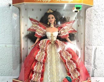 May include: A red and white Barbie doll wearing a gold crown and a red and white gown with gold trim. The doll is in a clear plastic box with a red and gold background. The box says "Happy Holidays" and "Special Edition Barbie".