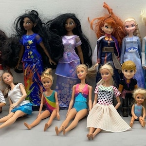 Puede incluir: Una colecci&oacute;n de 14 mu&ntilde;ecas, incluyendo princesas de Disney, con varios peinados y atuendos. Las mu&ntilde;ecas est&aacute;n dispuestas en una fila sobre una superficie blanca.