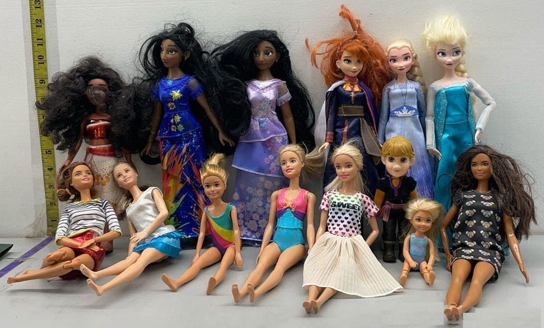 Puede incluir: Una colecci&oacute;n de 14 mu&ntilde;ecas, incluyendo princesas de Disney, con varios peinados y atuendos. Las mu&ntilde;ecas est&aacute;n dispuestas en una fila sobre una superficie blanca.