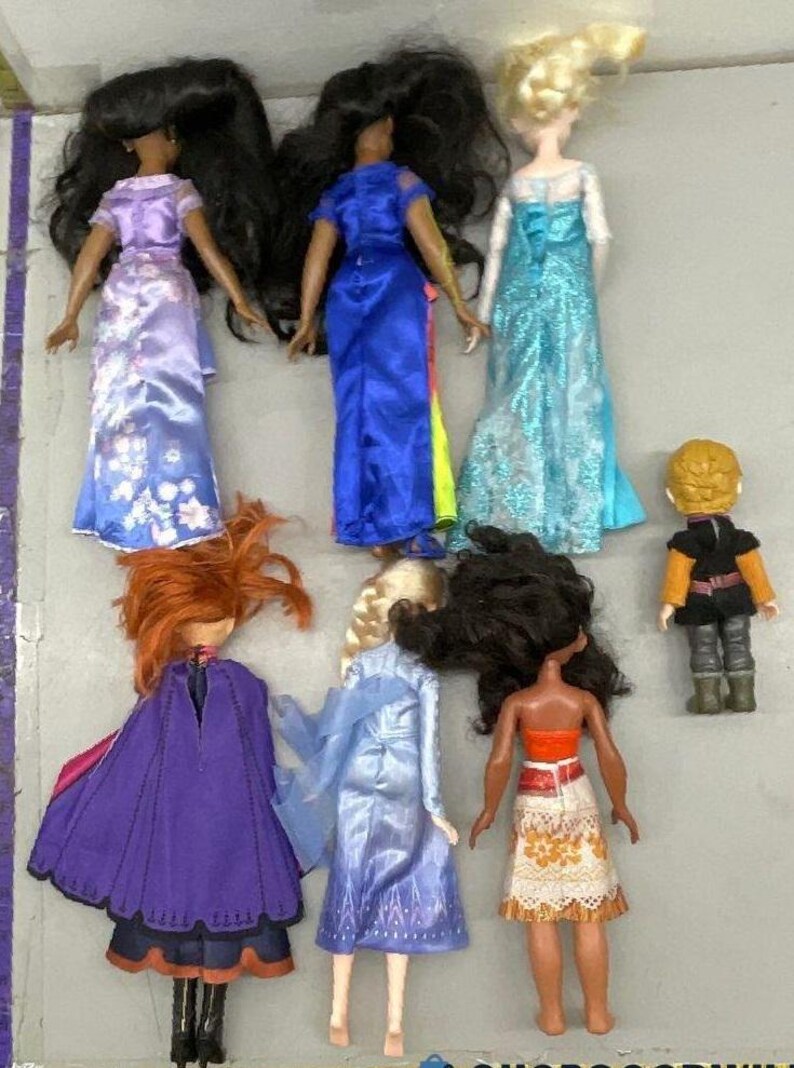 Puede incluir: Una colecci&oacute;n de ocho mu&ntilde;ecas, incluyendo princesas, una reina y un pr&iacute;ncipe. Las mu&ntilde;ecas llevan todas diferentes atuendos, incluyendo un vestido azul, un vestido morado, un vestido blanco, un vestido rojo, un vestido amarillo, un vestido verde, un vestido marr&oacute;n y un vestido negro.