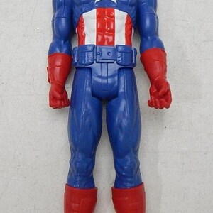 May include: A blue and red plastic action figure of Captain America. The figure has a red, white, and blue costume with a star on the chest. The figure is standing with its arms at its sides.