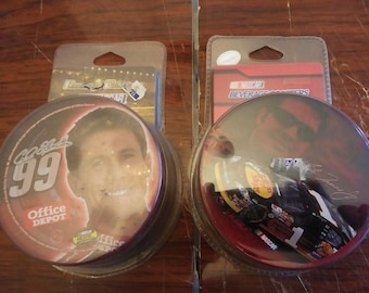May include: Two round, clear plastic coasters with images inside. One coaster features a red background with a photo of a race car driver and a race car. The text "NASCAR BEVERAGE COASTERS" is printed on the card behind the coaster. The other coaster features a red background with a photo of a man and the text "Gordon 99 Office Depot".