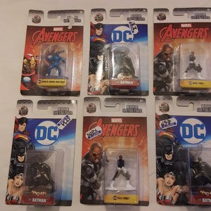 May include: Six packaged Marvel Avengers and DC Comics figurines. The figurines are in clear plastic cases attached to cardboard backings. The packaging features the Marvel Avengers and DC Comics logos, along with character names like Batman and Nick Fury.