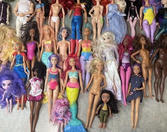 May include: A collection of dolls with various hairstyles, outfits, and accessories. The dolls are arranged in a row on a light-colored surface. Some of the dolls are wearing dresses, while others are wearing pants or skirts. The dolls have different hair colors, including blonde, brown, black, and red.