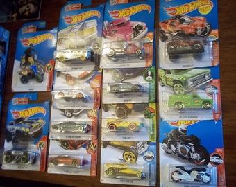 May include: A collection of Hot Wheels toy cars and motorcycles in their original packaging. The vehicles are in various colors, including red, green, yellow, and blue. The packaging features the Hot Wheels logo and vehicle names.