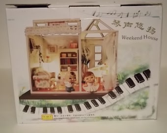 May include: A white box with a picture of a miniature dollhouse on the front. The dollhouse is decorated with a lace curtain and a piano. The box has the text "Weekend House" and "琴声悠扬" printed on it.