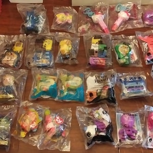 Puede incluir: Una colecci&oacute;n de 24 bolsas de pl&aacute;stico que contienen varios juguetes y baratijas. Los juguetes son en su mayor&iacute;a peque&ntilde;os y coloridos, y est&aacute;n empaquetados en bolsas de pl&aacute;stico transparentes con etiquetas blancas. Algunos de los juguetes incluyen un coche azul, una varita rosa, un personaje amarillo y un personaje verde.