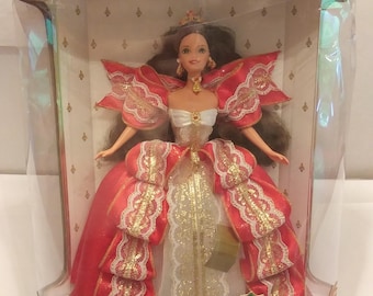 May include: A Barbie doll in a clear plastic box. The doll is wearing a red and gold gown with a white bodice. The box has the words "Happy Holidays" and "Special Edition Barbie" printed on it.