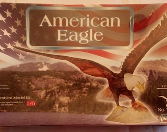 May include: A model kit of an American Bald Eagle in flight. The box art features a close-up of the eagle with a 12-inch wingspan. The kit is 1/6 scale and is recommended for ages 10 and over. The box is red, white, and blue with the words "American Eagle" in a silver rectangle. The box also includes the Lindberg logo and the model number 70315.