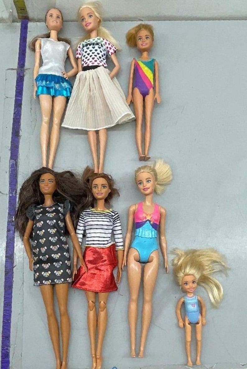 Puede incluir: Siete mu&ntilde;ecas Barbie con diferentes atuendos, que incluyen una blusa blanca con una falda azul, un vestido de lunares blanco y negro, una camisa a rayas con una falda roja, un traje de ba&ntilde;o azul, un traje de ba&ntilde;o arco&iacute;ris, un traje de ba&ntilde;o rosa y azul y un traje de ba&ntilde;o azul. Las mu&ntilde;ecas tienen diferentes colores y estilos de cabello.