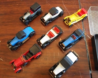 May include: A collection of eight vintage toy cars in various colors, including red, blue, yellow, white, and black. The cars are all in a classic style, with open tops and detailed features.