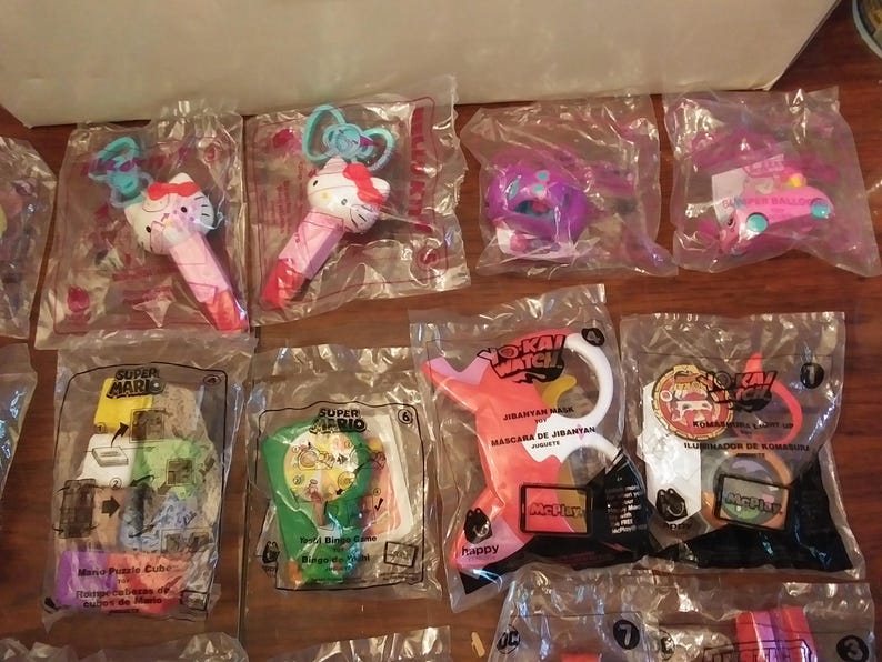 Puede incluir: Surtido de envases de personajes de juguetes coloridos, incluyendo Super Mario, Yo-Kai Watch y Hello Kitty. Los envases son de pl&aacute;stico transparente y presentan varios personajes y logotipos.