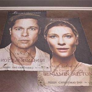 Könnte beinhalten: Zwei Filmplakate für den Film "Der seltsame Fall des Benjamin Button" mit Brad Pitt und Cate Blanchett. Beide Poster sind weiß mit schwarzem Text und zeigen den Filmtitel und das Erscheinungsdatum.
