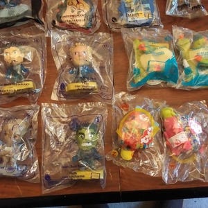 Puede incluir: Una colecci&oacute;n de 10 figuras de juguete de pl&aacute;stico en envases de pl&aacute;stico transparente. Las figuras incluyen personajes de pel&iacute;culas y programas de televisi&oacute;n populares, como Thor, Hulk y personajes de la pel&iacute;cula de Lego. El envase es morado y presenta el nombre del personaje y una peque&ntilde;a imagen del personaje.