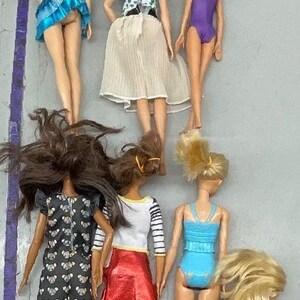 Puede incluir: Una colecci&oacute;n de ocho mu&ntilde;ecas con diferentes peinados y atuendos. Las mu&ntilde;ecas llevan una variedad de ropa, incluidos vestidos, faldas y trajes de ba&ntilde;o. Todas las mu&ntilde;ecas est&aacute;n de pie sobre una superficie gris claro.