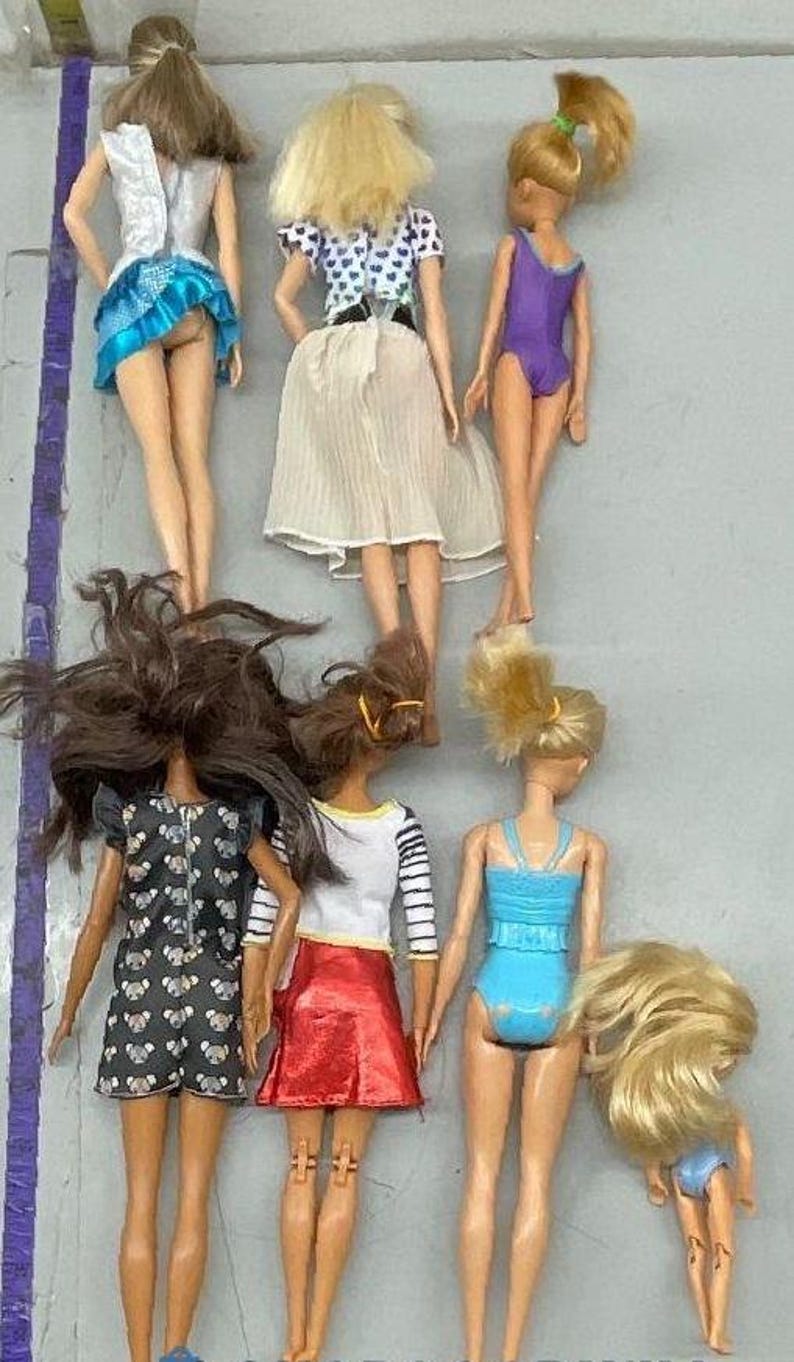Puede incluir: Una colecci&oacute;n de ocho mu&ntilde;ecas con diferentes peinados y atuendos. Las mu&ntilde;ecas llevan una variedad de ropa, incluidos vestidos, faldas y trajes de ba&ntilde;o. Todas las mu&ntilde;ecas est&aacute;n de pie sobre una superficie gris claro.