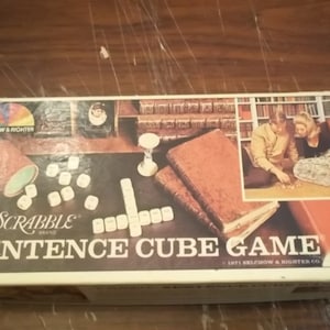 May include: A vintage Scrabble Sentence Cube Game box with a colourful rainbow logo and the text "Scrabble Sentence Cube Game" on the front. The box features a picture of two people playing the game with dice and a timer.