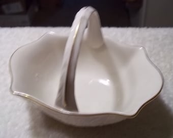 May include: A white porcelain basket with a gold trim and a handle. The basket is shaped like a flower and has a scalloped edge.