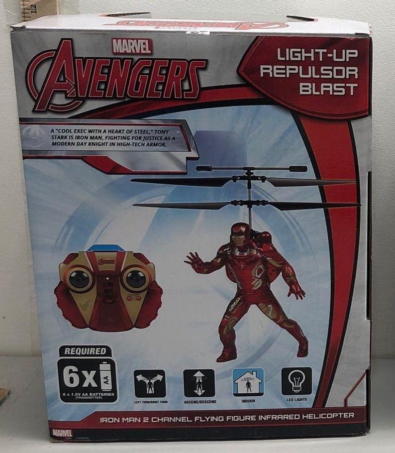 May include: A red and gold Iron Man flying figure infrared helicopter toy with a light-up repulsor blast. The box shows a red and gold remote control and the text "A 'cool exec with a heart of steel' - Tony Stark is Iron Man, fighting for justice as a modern day knight in high-tech armor."  The box also says "Required 6x 1.5V AA batteries".