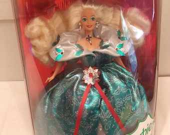 May include: A Barbie doll in a clear plastic case. The doll is wearing a teal and silver gown with a red ribbon and a jeweled brooch. The case has the words "Happy Holidays" and "Special Edition" printed on it.