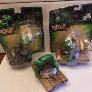以下が含まれることがあります： 3体のハルクのアクションフィギュア。2体のフィギュアはオリジナルのパッケージに入っており、「SMASH & GO HULK with PUNCHING ACTION!」と書かれています。3体目のフィギュアはミニチュア戦車の上にポーズをとっています。フィギュアは緑と茶色です。