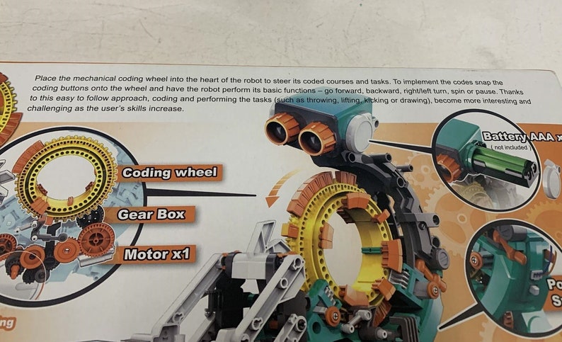 Puede incluir: Un robot de juguete verde, amarillo y naranja con una rueda de codificaci&oacute;n. La rueda de codificaci&oacute;n es un engranaje circular con una serie de botones que se pueden usar para programar el robot. El robot tambi&eacute;n tiene una caja de engranajes y un motor. El texto en la imagen dice: "Coloque la rueda de codificaci&oacute;n mec&aacute;nica en el coraz&oacute;n del robot para dirigir sus cursos y tareas codificados. Para implementar los c&oacute;digos, encaje los botones de codificaci&oacute;n en la rueda y haga que el robot realice sus funciones b&aacute;sicas: avanzar, retroceder, girar a la derecha/izquierda, girar o pausar. Gracias a este enfoque f&aacute;cil de seguir, la codificaci&oacute;n y la realizaci&oacute;n de las tareas (como lanzar, levantar, patear o dibujar) se vuelven m&aacute;s interesantes y desafiantes a medida que las habilidades del usuario aumentan. Bater&iacute;a AAA (no incluida)"
