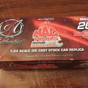 Könnte beinhalten: Eine rot-weiß-schwarze Box mit einer 1:24-Maßstabs-Die-Cast-Stock-Car-Replik des NASCAR #26 Mac Tools Autos. Die Box zeigt das Mac Tools Motorsports Logo, das Betty Crocker Logo und die Worte "Authentics" und "Limited Edition".