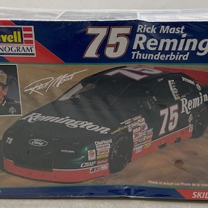 Puede incluir: Una caja de kit de modelo de coche que presenta un coche de carreras NASCAR de los años 90 de color verde y negro con el número 75 y el nombre "Remington" en el lateral. La caja también presenta el nombre "Rick Mast" y el texto "75 Remington Thunderbird".