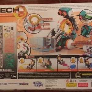 Puede incluir: Un kit de robot de codificaci&oacute;n mec&aacute;nica verde y naranja con las palabras 'Mech 5' y 'Teach Tech' en la caja. El robot tiene una rueda de codificaci&oacute;n, una caja de engranajes y un motor. La caja tambi&eacute;n incluye herramientas e instrucciones.