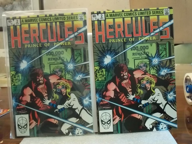 以下が含まれることがあります： 「Hercules, Prince of Power」というタイトルの2冊のコミック。表紙には、筋肉質な男性と白い衣装の女性が描かれており、Marvel Comicsのロゴがあります。背景には「100,000 REWARD」の文字が含まれています。