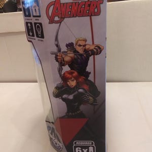 May include: A cardboard box for a Marvel Avengers toy. The box features a red, white and black design with images of Hawkeye and Black Widow. The text "MARVEL AVENGERS" is printed in large, bold letters on the box. The box also includes the text "REQUIRED 6x AA BATTERIES".