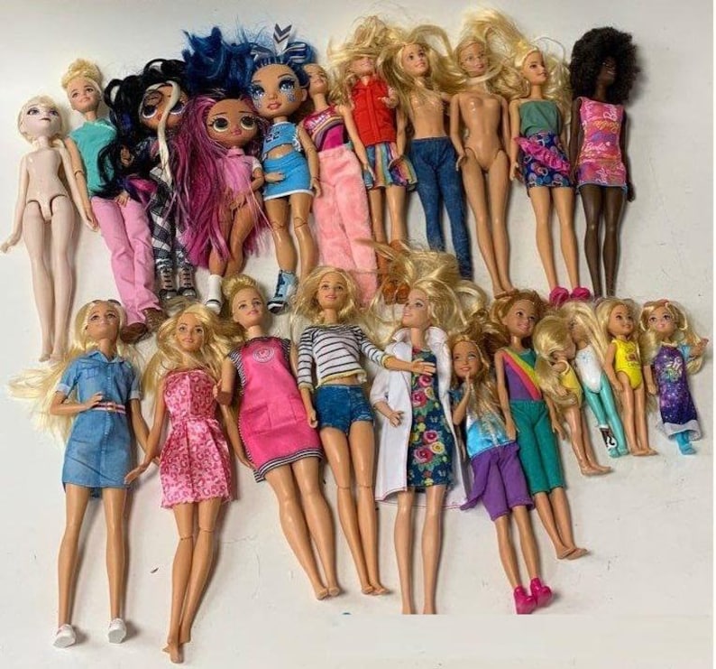 May include: A collection of 19 dolls, including Barbie dolls, fashion dolls, and other dolls. The dolls are dressed in a variety of colorful outfits, including dresses, skirts, pants, and shirts. Some dolls have long hair, while others have short hair. The dolls are all standing on a white surface.