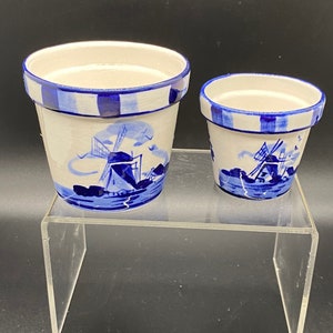 May include: Two blue and white ceramic flower pots with a windmill design. The larger pot is 4 inches tall and the smaller pot is 3 inches tall.