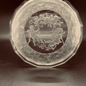 May include: A clear glass dish with a raised design of cherubs and roses. The dish has a scalloped edge and is perfect for holding small items.