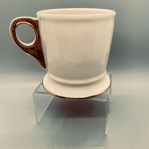 Puede incluir: Una taza de cer&aacute;mica blanca con asa y borde dorados. La taza tiene un dise&ntilde;o cl&aacute;sico con una forma ligeramente acampanada y una base de pedestal. El asa es de un color contrastante, agregando un toque de elegancia al dise&ntilde;o.
