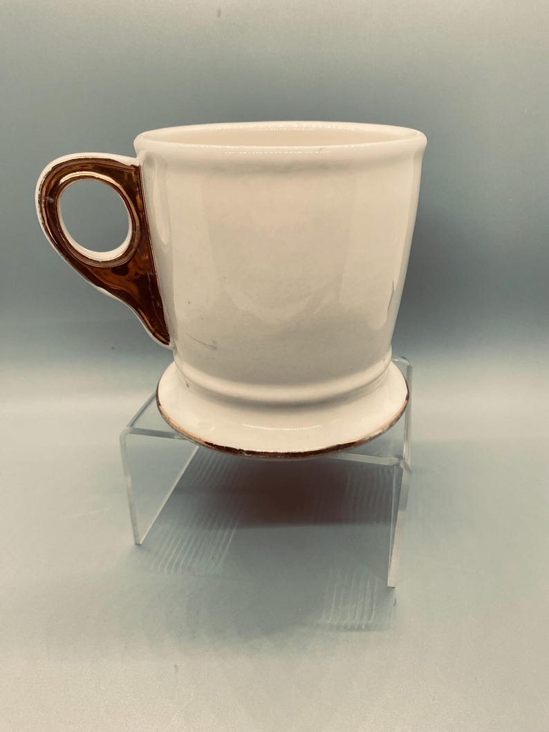 Puede incluir: Una taza de cer&aacute;mica blanca con asa y borde dorados. La taza tiene un dise&ntilde;o cl&aacute;sico con una forma ligeramente acampanada y una base de pedestal. El asa es de un color contrastante, agregando un toque de elegancia al dise&ntilde;o.