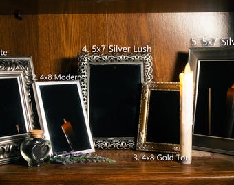 May include: Five different picture frames with ornate silver and gold finishes, arranged on a wooden shelf. The frames are all different sizes and styles, and some have mirrors inside. A candle is placed in front of the frames.