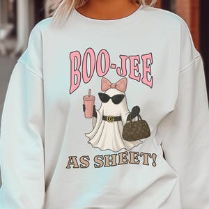 May include: White sweatshirt with a graphic that says "BOO-JEE AS SHEET!". The graphic features a ghost wearing sunglasses, a bow, and holding a drink and a purse.