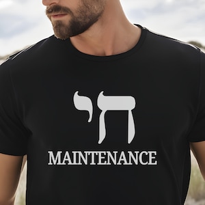 May include: Black t-shirt with a white graphic of the Hebrew word "Chai" and the word "MAINTENANCE" below it. The shirt is a crew neck style.