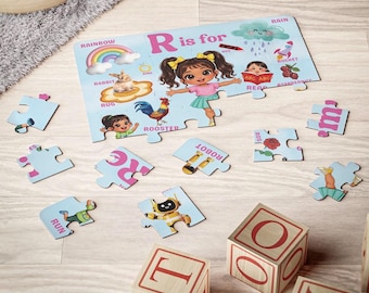 May include: A children's alphabet puzzle featuring the letter R with illustrations of a rainbow, rabbit, rug, rooster, rain, rocket, and raspberries. A central character with pigtails is shown alongside text reading R is for. Loose puzzle pieces are scattered.