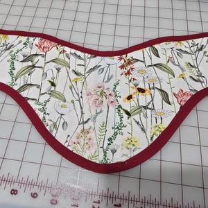 May include: A floral-patterned fabric piece with a curved shape, featuring a white background with colorful flowers and green foliage. The edges are trimmed with a deep red fabric. The text "November 16, 2023 10:51 AM" is visible in the upper left corner.