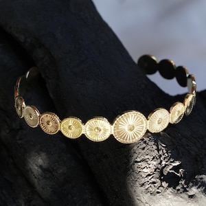 May include: A gold bangle bracelet with a repeating pattern of small, circular, embossed medallions.