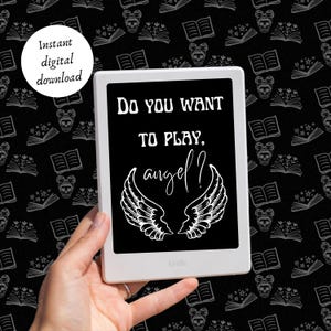 以下が含まれることがあります： 「Do you want to play. angel?」というテキストが画面に表示された白黒のデジタルリーダー。リーダーは、本、星、頭蓋骨が繰り返し描かれた黒い背景に映し出され、手で持たれている。