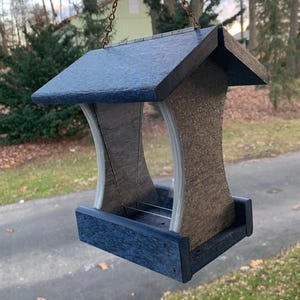 May include: A blue and brown bird feeder with a roof and a hanging chain. The feeder has a rectangular base and two curved sides.