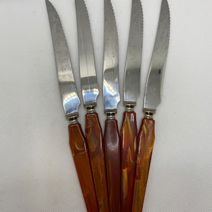Puede incluir: Juego de cinco cuchillos para carne de acero inoxidable con mangos de plástico marmoleado marrón y dorado.