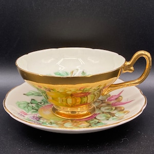 Taylor & Kent tekopp med fat. Guldfärgad utsida och kanter, transferware med fruktmotiv. Gratulationsfärgad och med fot. Vintage Storbritannien från 1950-talet. Har repor.