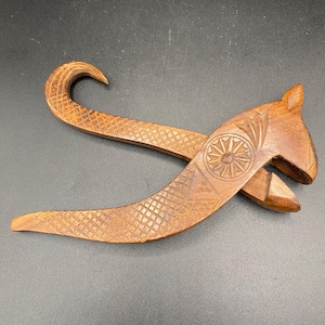 Può includere: Un schiaccianoci di legno intagliato a forma di scoiattolo. Lo schiaccianoci è marrone e presenta dettagli intricati, tra cui un fiore intagliato sulla testa.