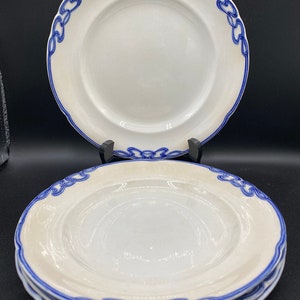 Puede incluir: Un juego de cuatro platos de cerámica blanca con un borde decorativo azul y blanco. Los platos tienen un borde ligeramente elevado y un acabado liso y brillante.