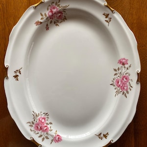 Puede incluir: Plato de cena de cerámica blanca con borde dorado y diseño floral rosa. El plato tiene un borde festoneado.