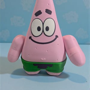 May include: A pink, starfish-shaped figurine with black eyes, eyebrows, and a smiling mouth. The figurine is wearing green shorts. The background is light blue with white cloud shapes.